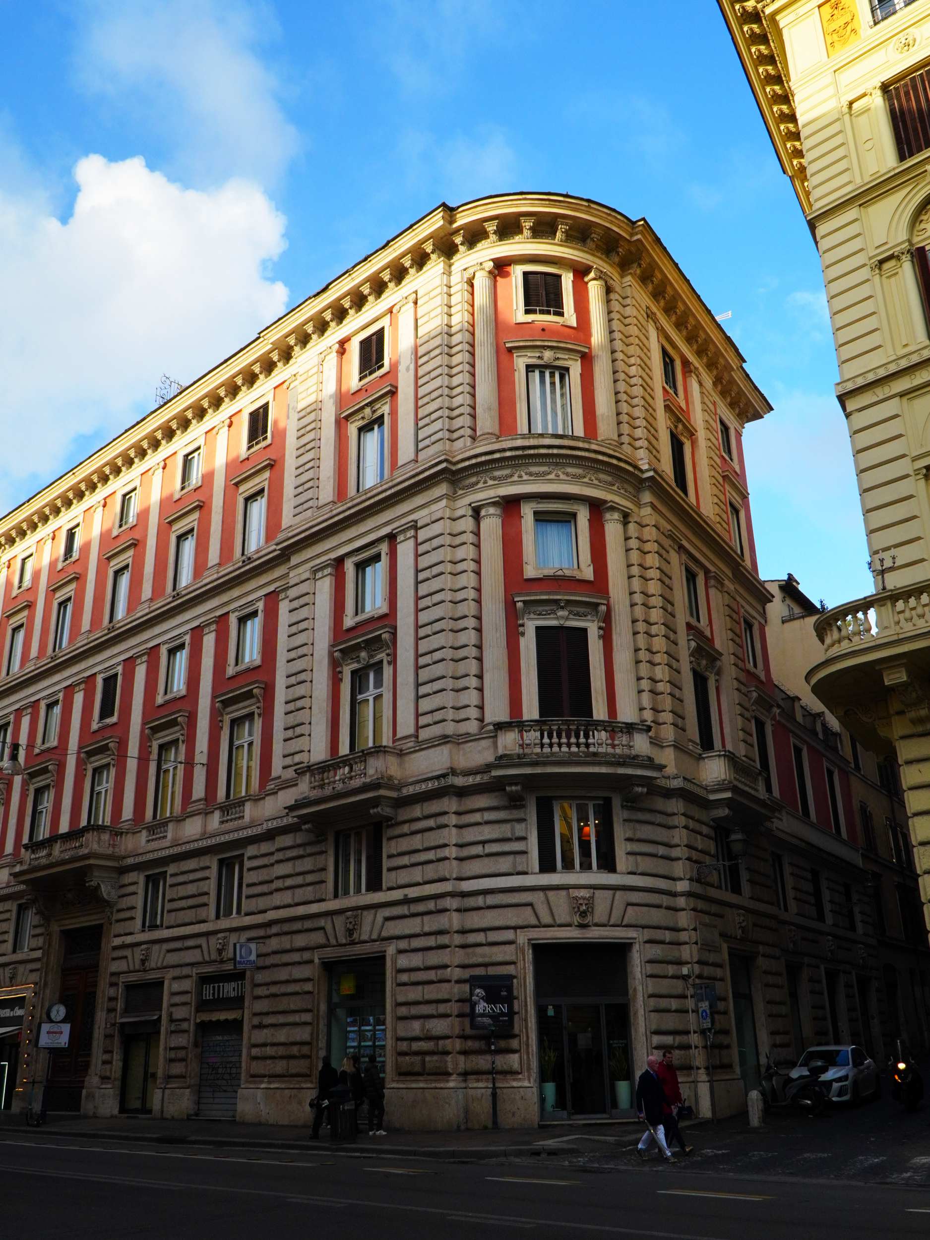 Un bâtiment historique à Rome, avec des façades ornées, colonnes et fenêtres décoratives, sous un ciel bleu avec quelques nuages.