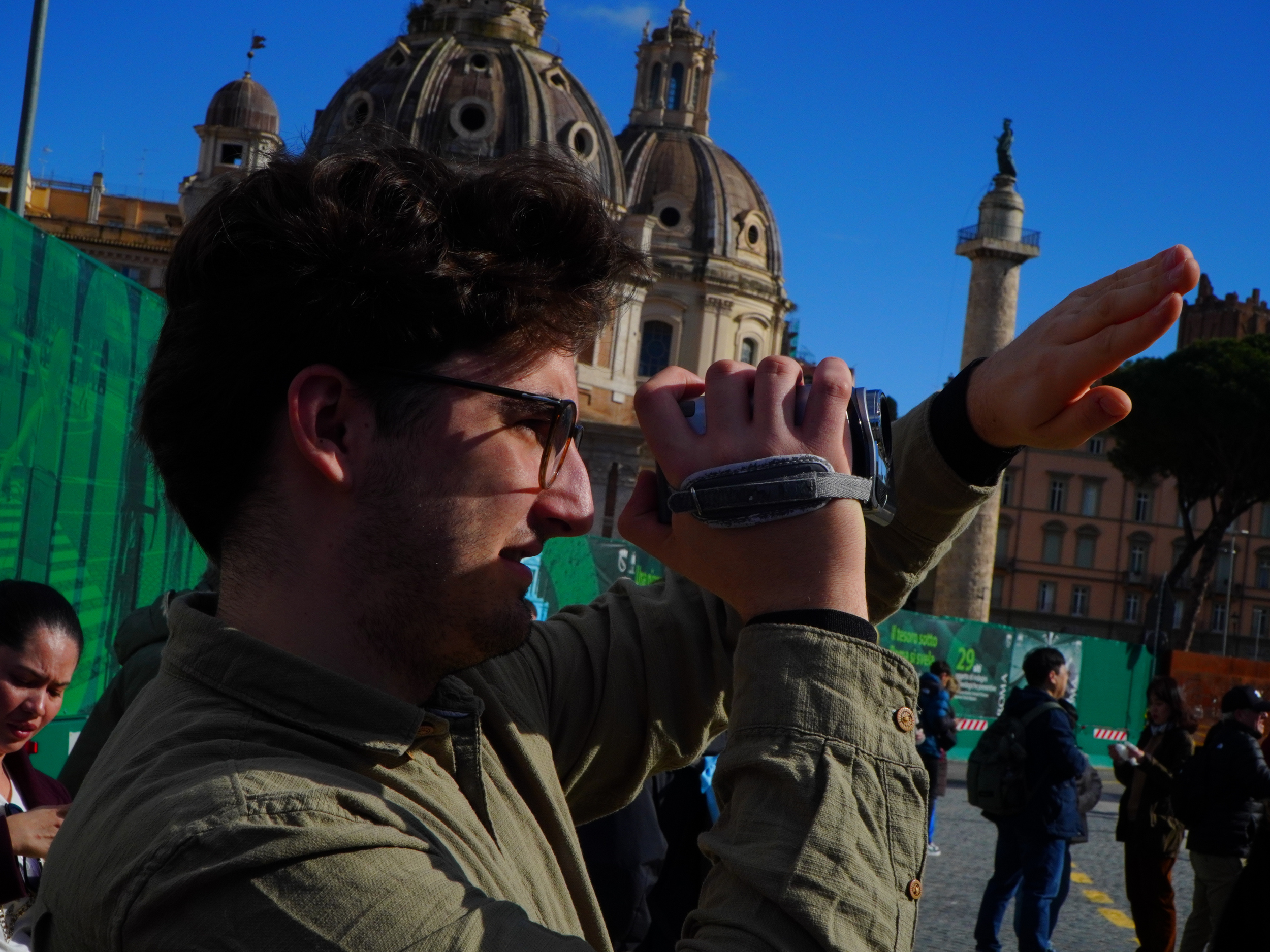 Un homme utilisant un appareil photo en extérieur avec une architecture religieuse en arrière-plan, sous un ciel bleu.