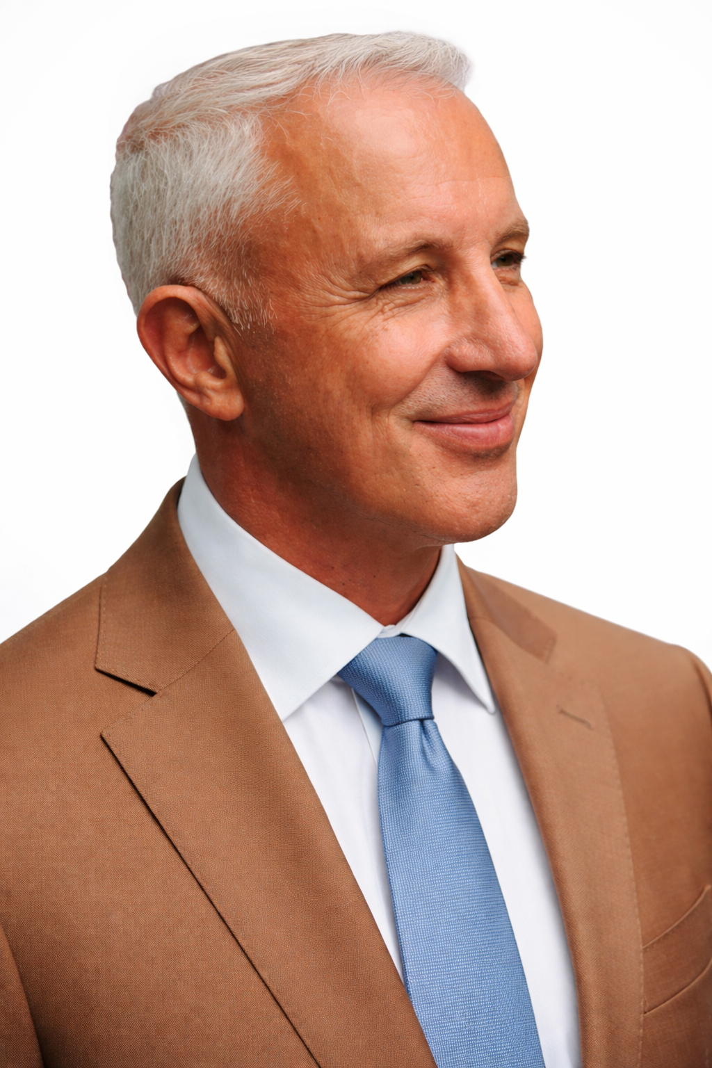 Close-up profile of a smiling middle-aged man with white hair, wearing a brown suit, white shirt, and blue tie against a white background.