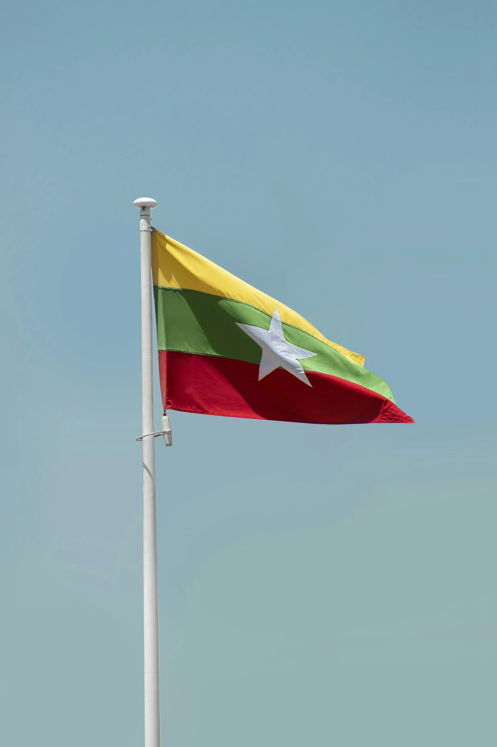A flag with yellow, green, and red horizontal stripes and a white star in the center of the green stripe, flying against a clear blue sky.
