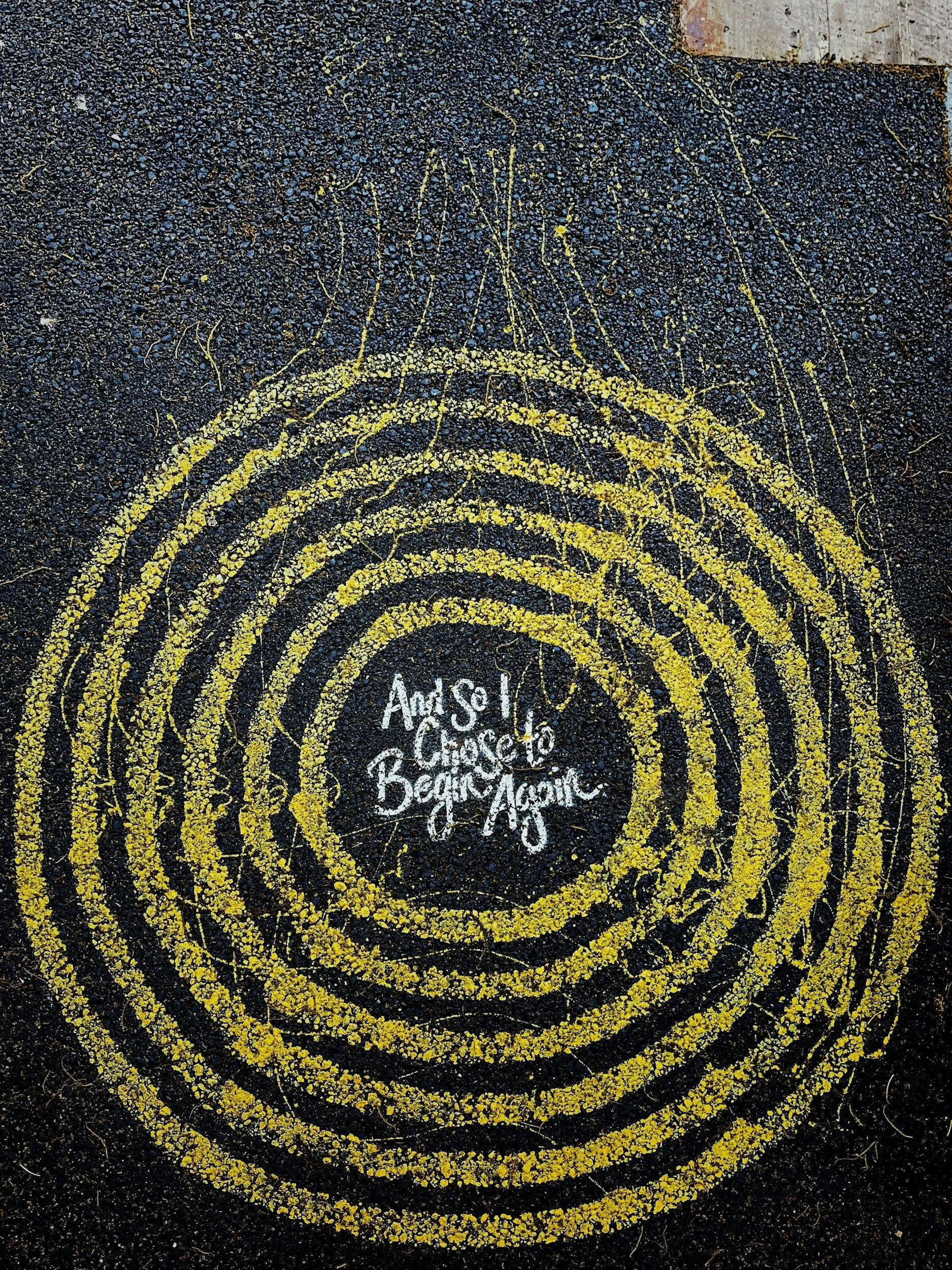 Street art on pavement with yellow circular lines and handwritten text that reads, 'Ask! Chat! Be Genuine!'