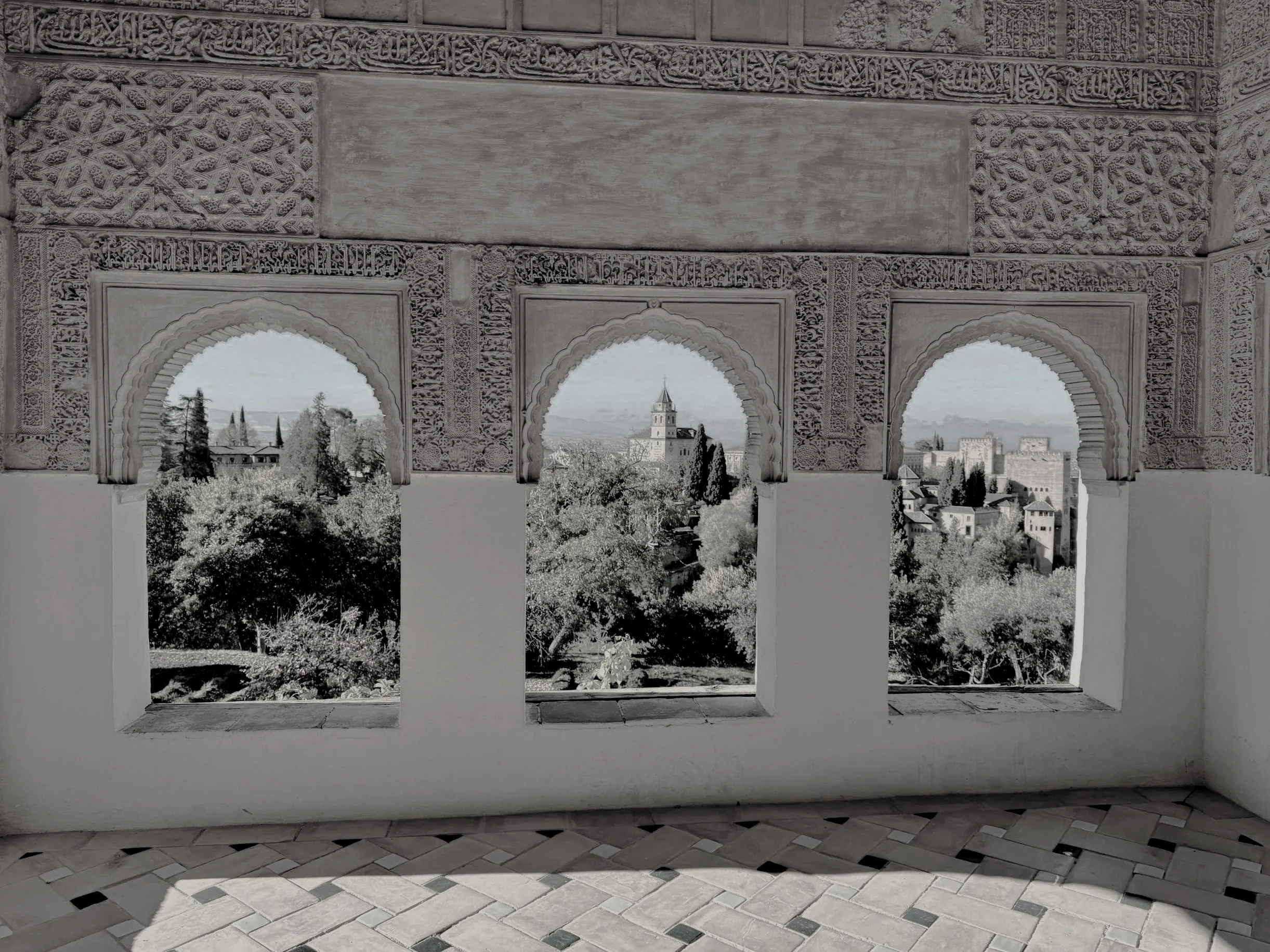 View through ornate arches showing a cityscape with a tower and trees, captured from a historic structure with intricate carvings.