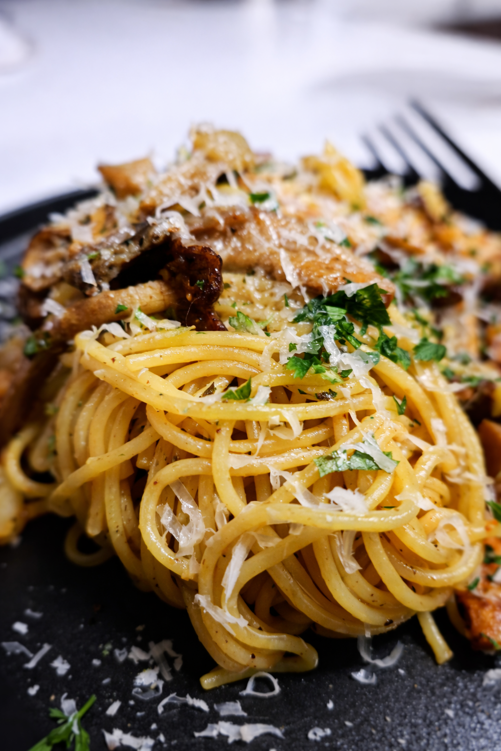Close-up of a plate of spaghetti with grated cheese, fresh parsley, and topped with pieces of cooked chicken.