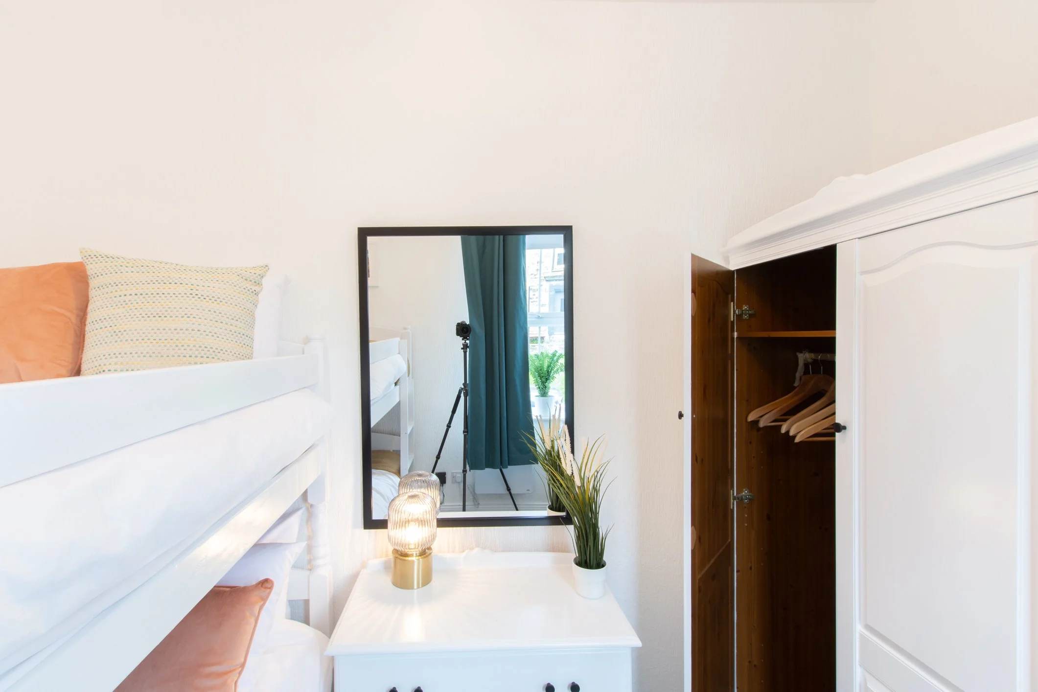 Interior of a bedroom with a loft bed, mirror, open closet, and decorative lamps.