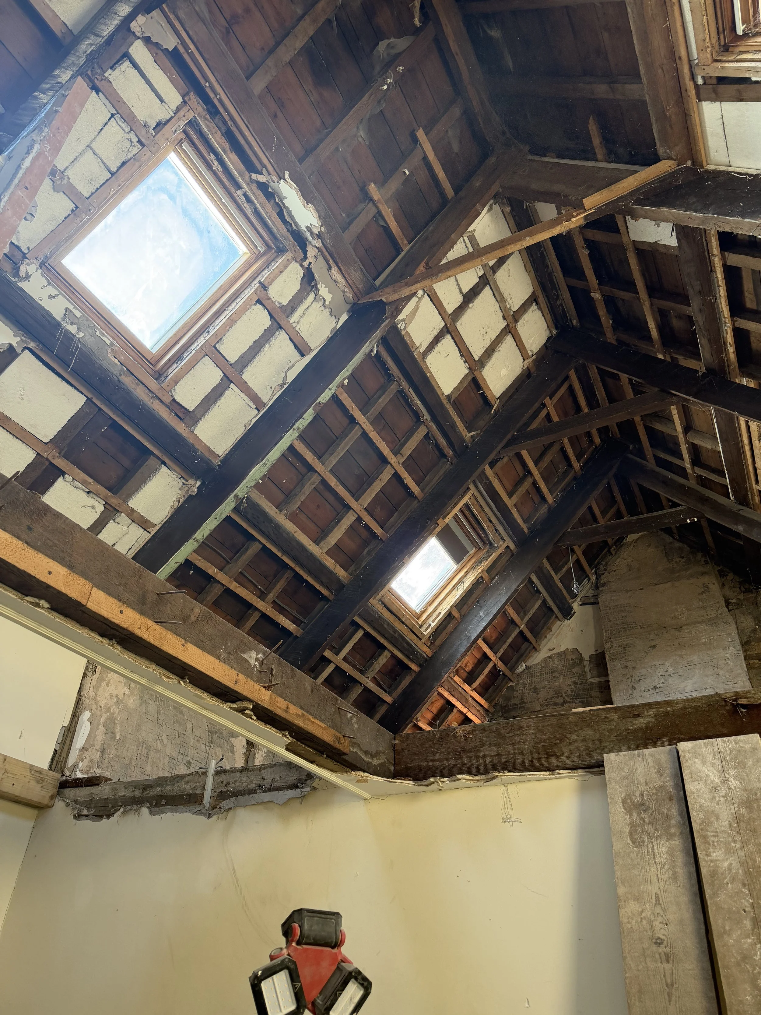 Attic with exposed wooden beams, two skylight windows, and construction tools, indicating renovation work.