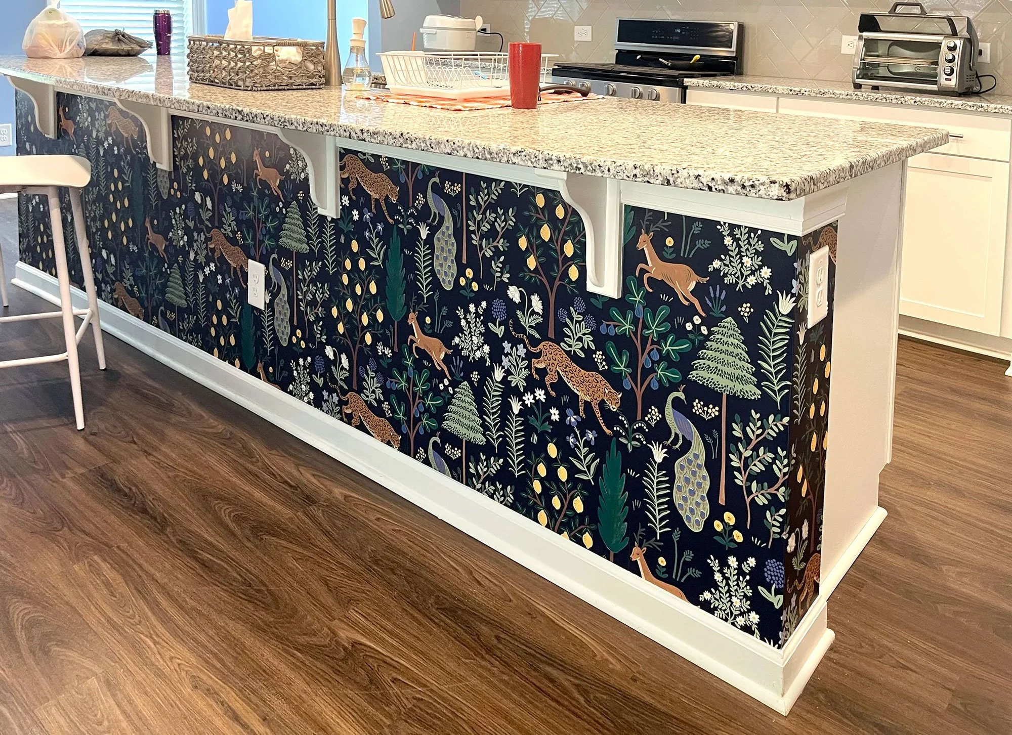 Kitchen island with a dark blue floral and wildlife pattern, featuring leopards, peacocks, and plants, contrasted with a white trim and a granite countertop.