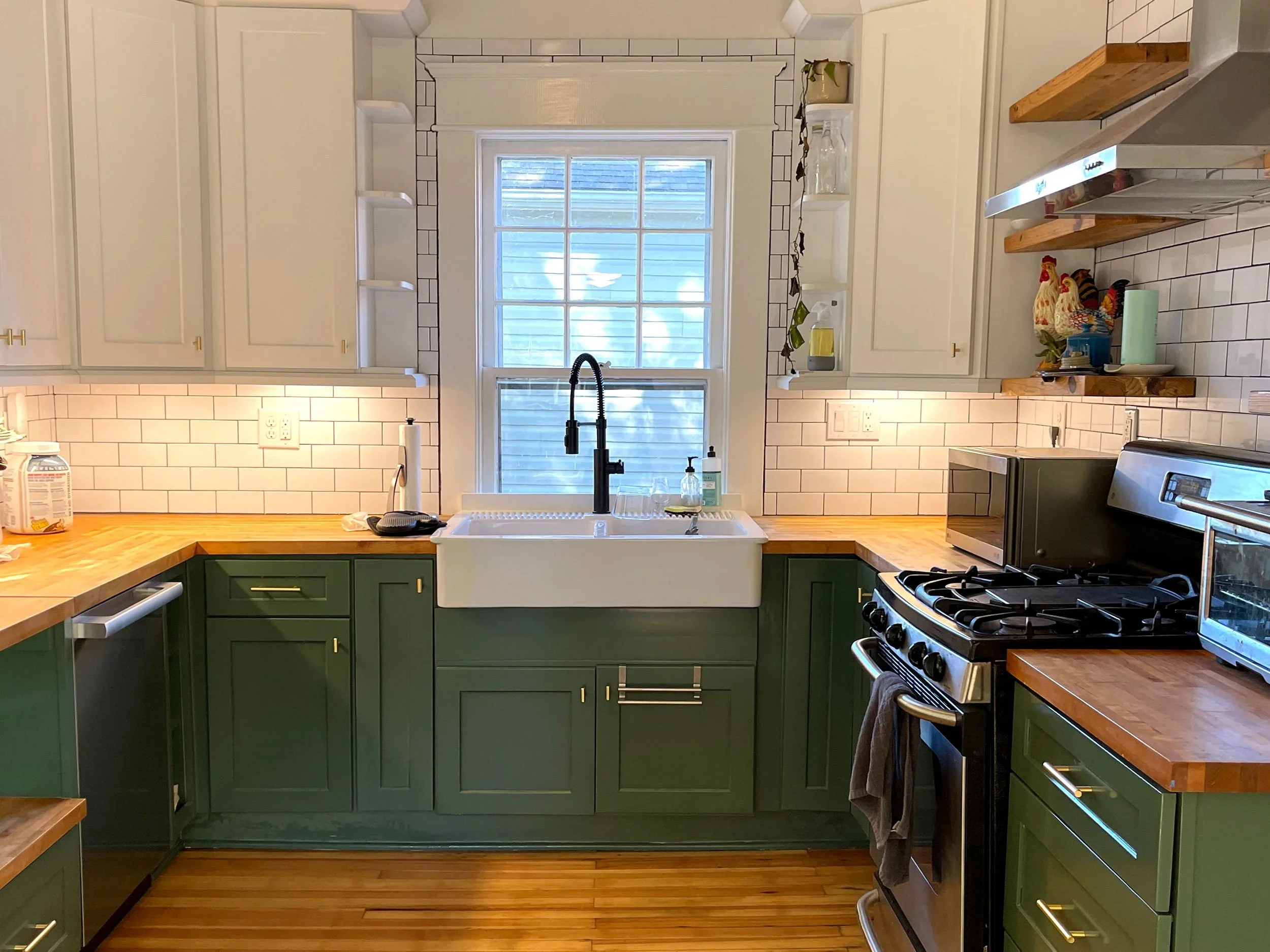A farmhouse like kitchen styled with two colors. White upper cabinets and green lower cabinets, and butcher block counter tops.