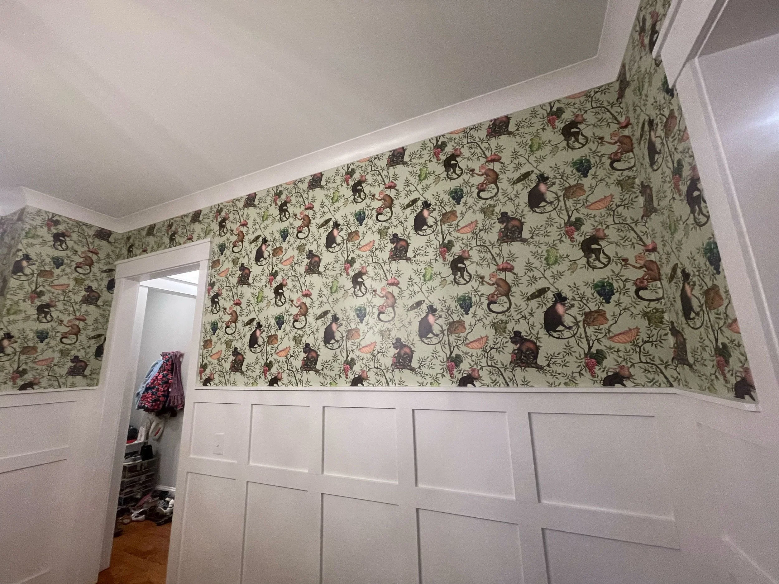 Room with white wainscoting and a wall covered in patterned wallpaper featuring monkeys and foliage.