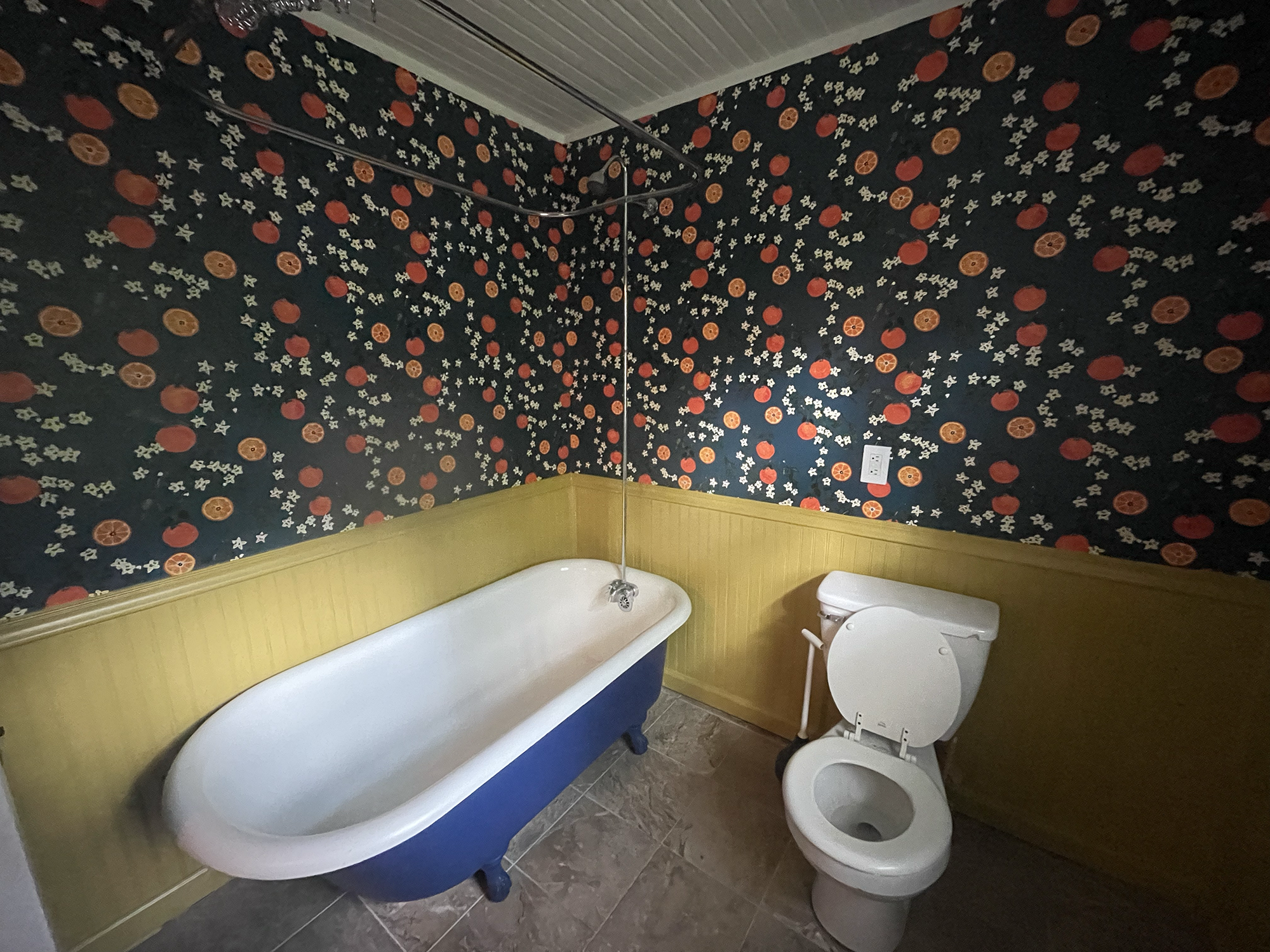 A bathroom with dark floral wallpaper, a bathtub, a toilet with the seat lid up, and a segment of a mirror.