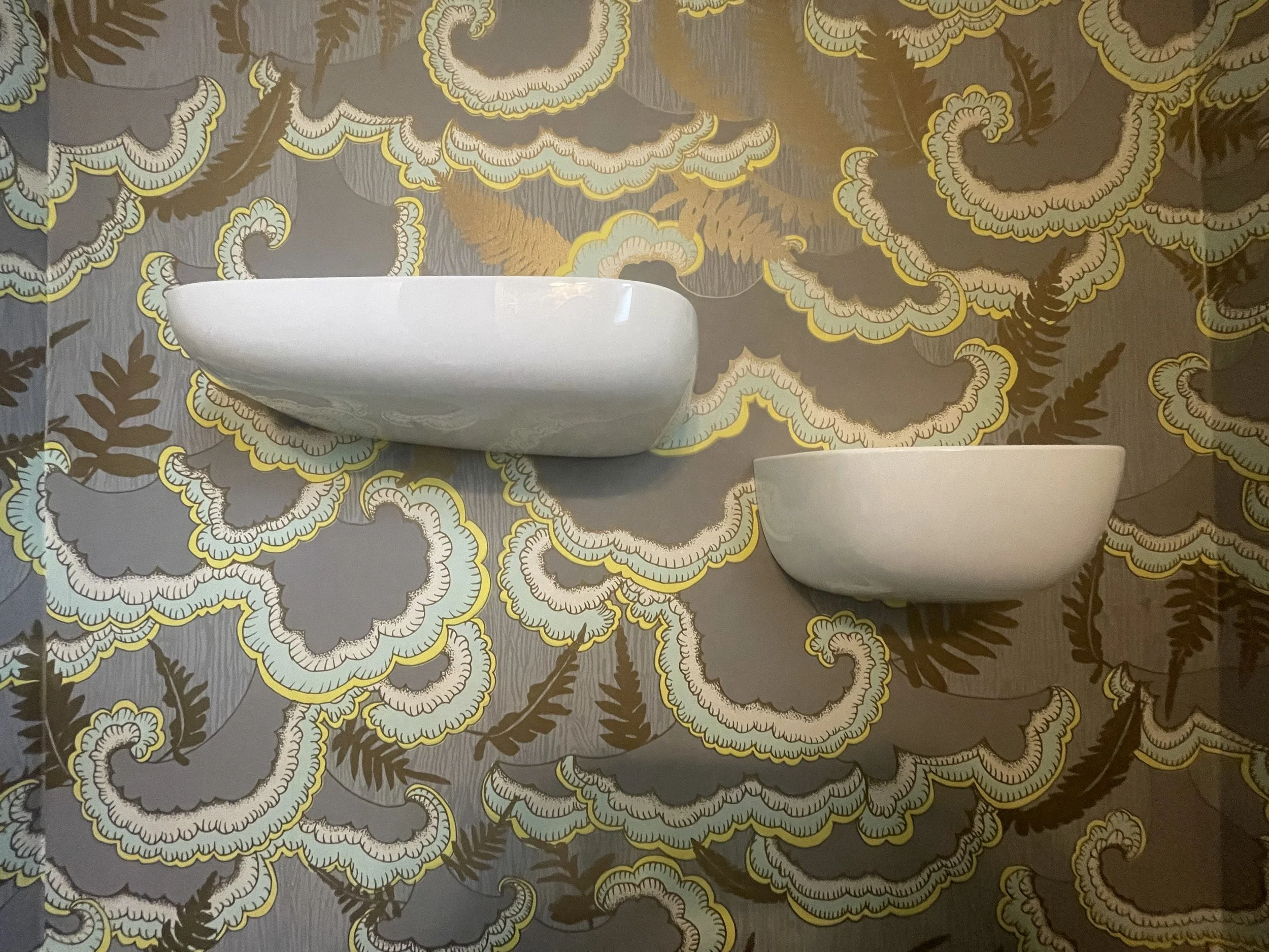 Close-up of a decorative wallpaper with a floral pattern in shades of gray, yellow, and light blue, featuring intricate cloud-like shapes and fern motifs.