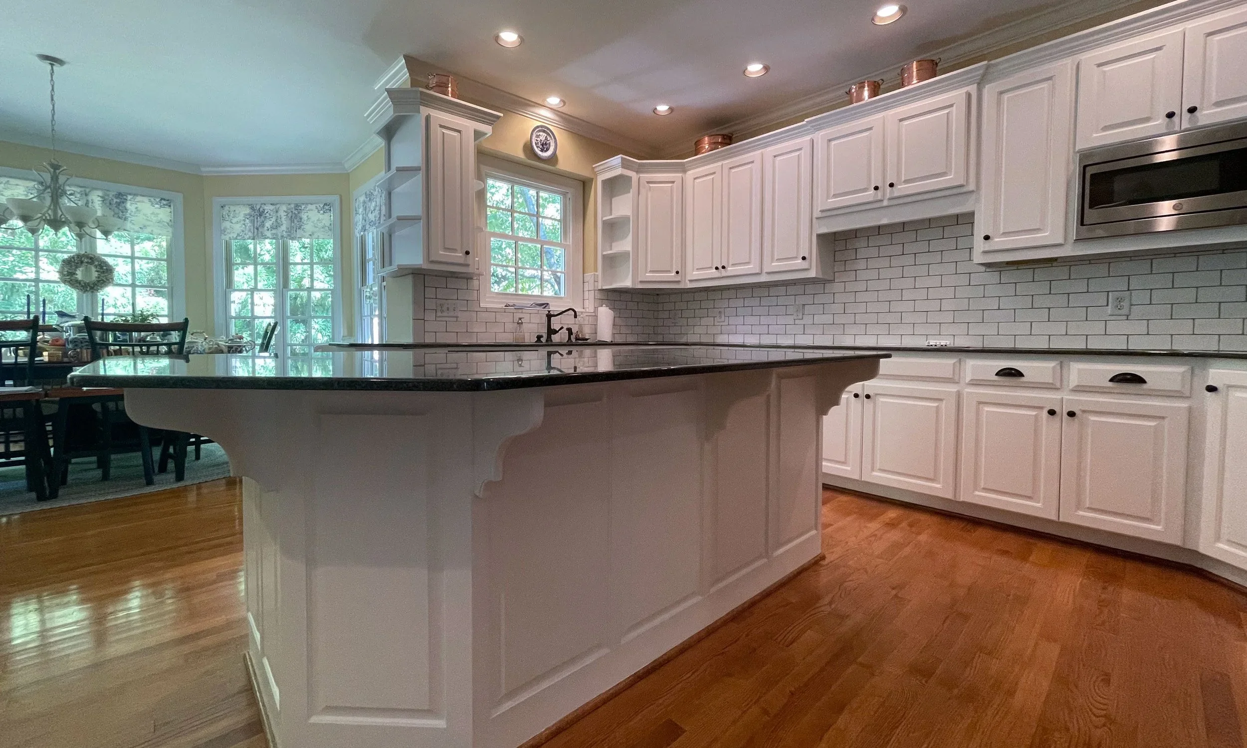 Kitchen with white cabinets, a black countertop island, hardwood floors, recessed lighting, and a window with a view of greenery.