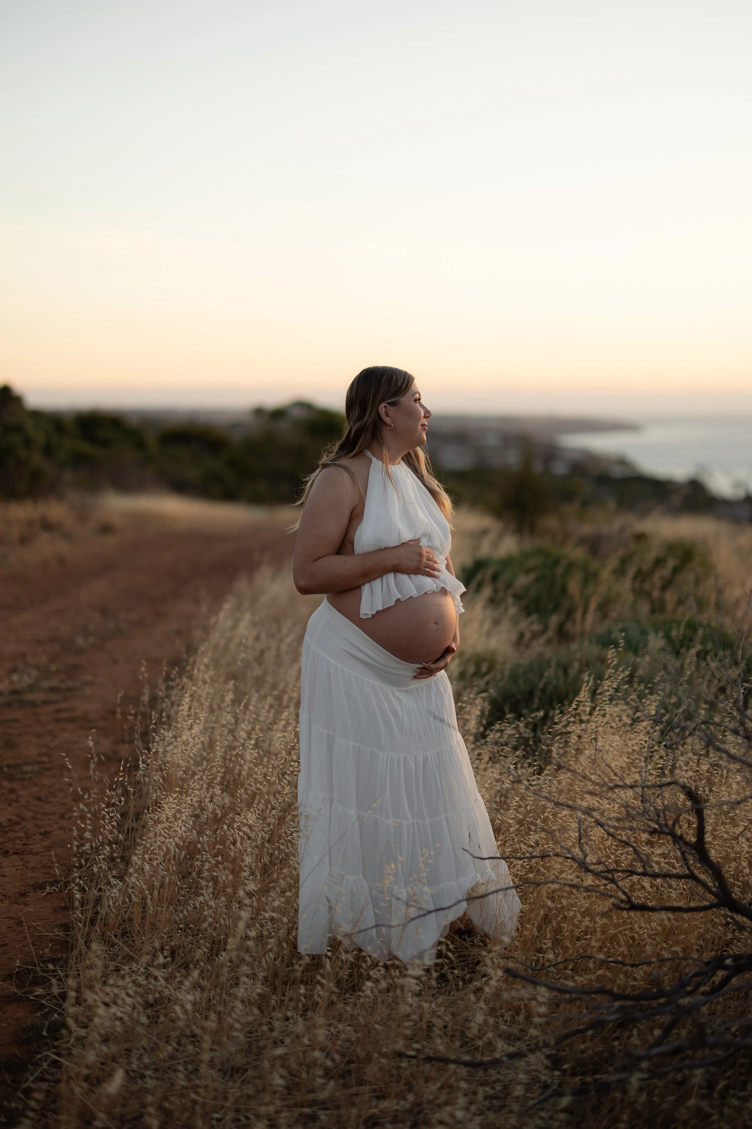 Pregnant woman standing on a coastal track at sunset during a maternity photography session in Adelaide.