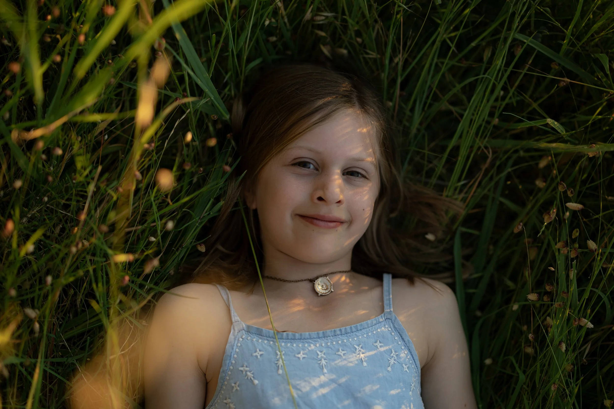 Portrait of a young girl lying in long grass during a family photography session in Adelaide.