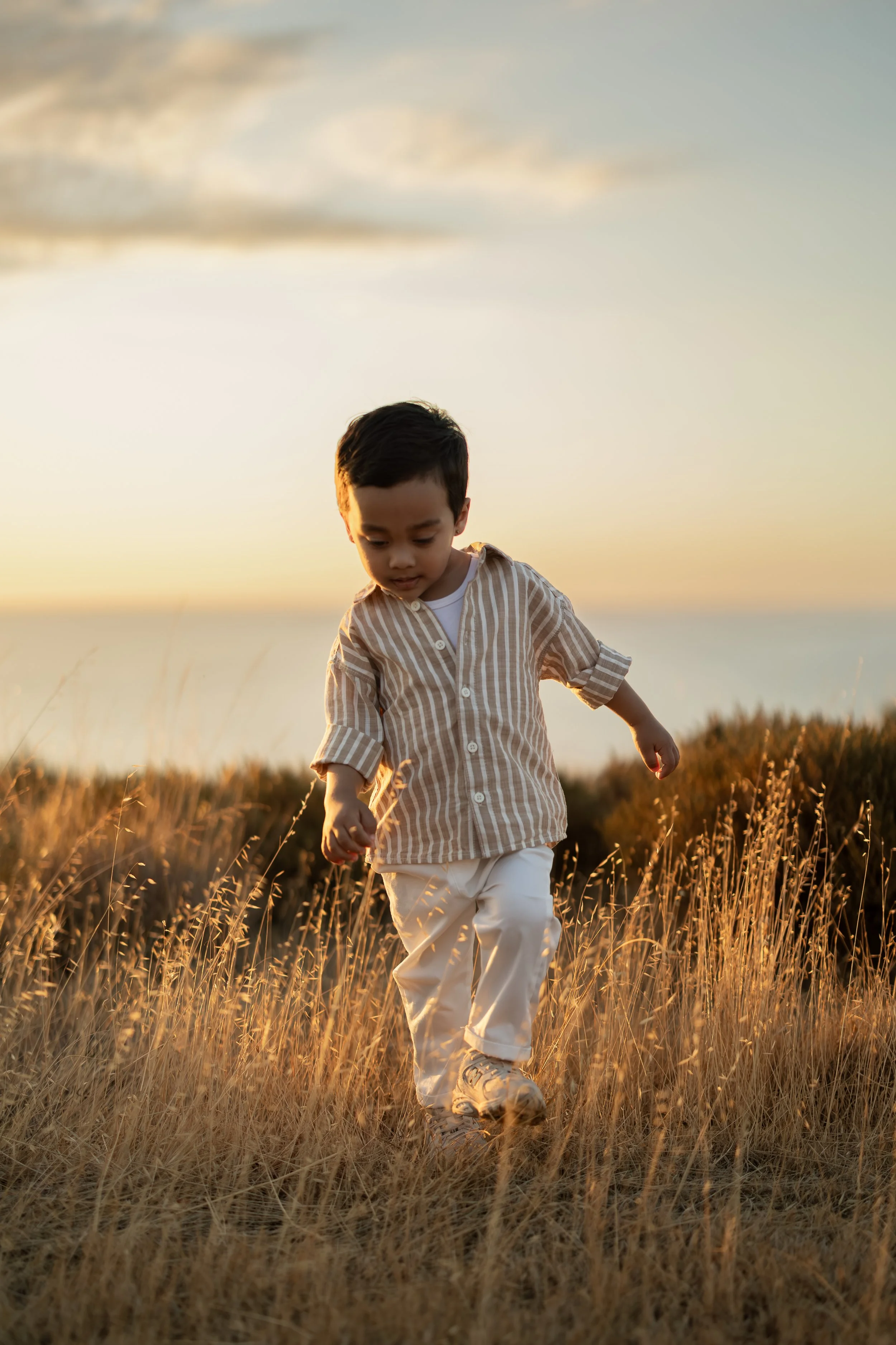 Young child walking through dry grass at sunset during a family photography session in Adelaide.
