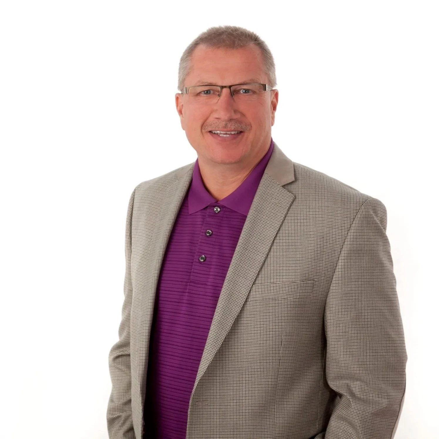 A middle-aged man with gray hair and glasses wearing a purple shirt and gray blazer, smiling against a plain white background.