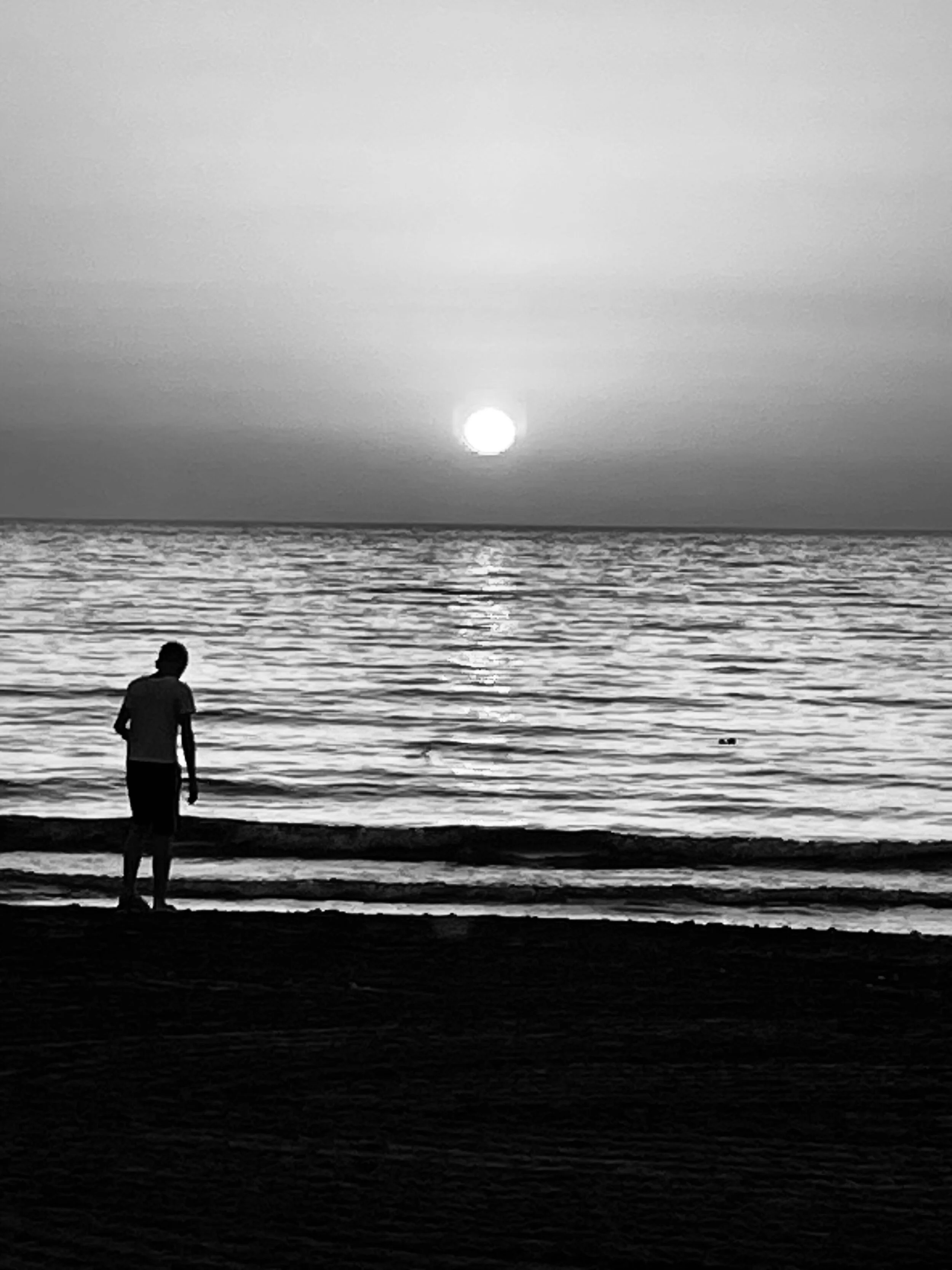 a black and white image of a boy playing on the beach as the sun goes down