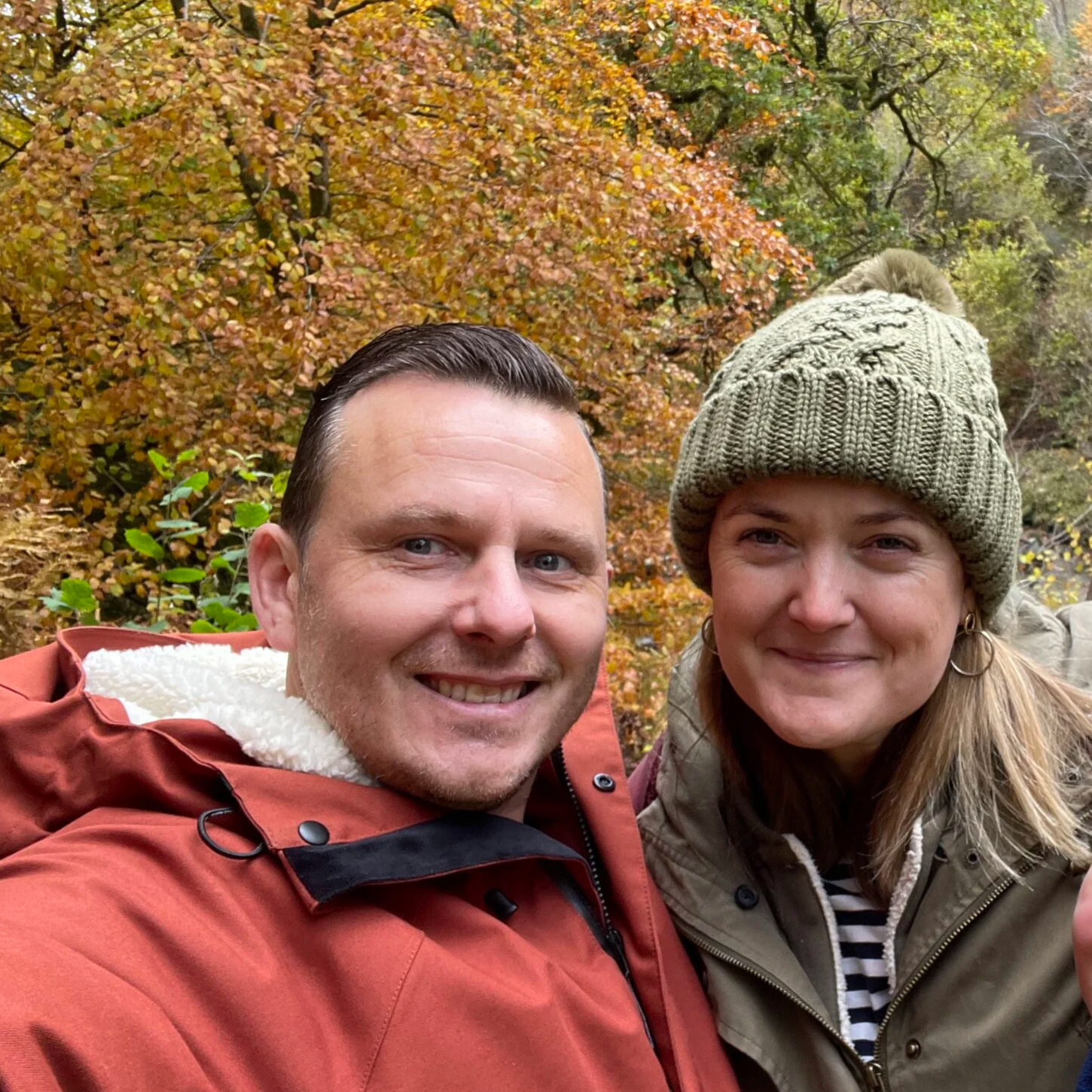 David and his wife Laura on a walk. He's wearing an orange coat and she is wearing a green coat and hat.