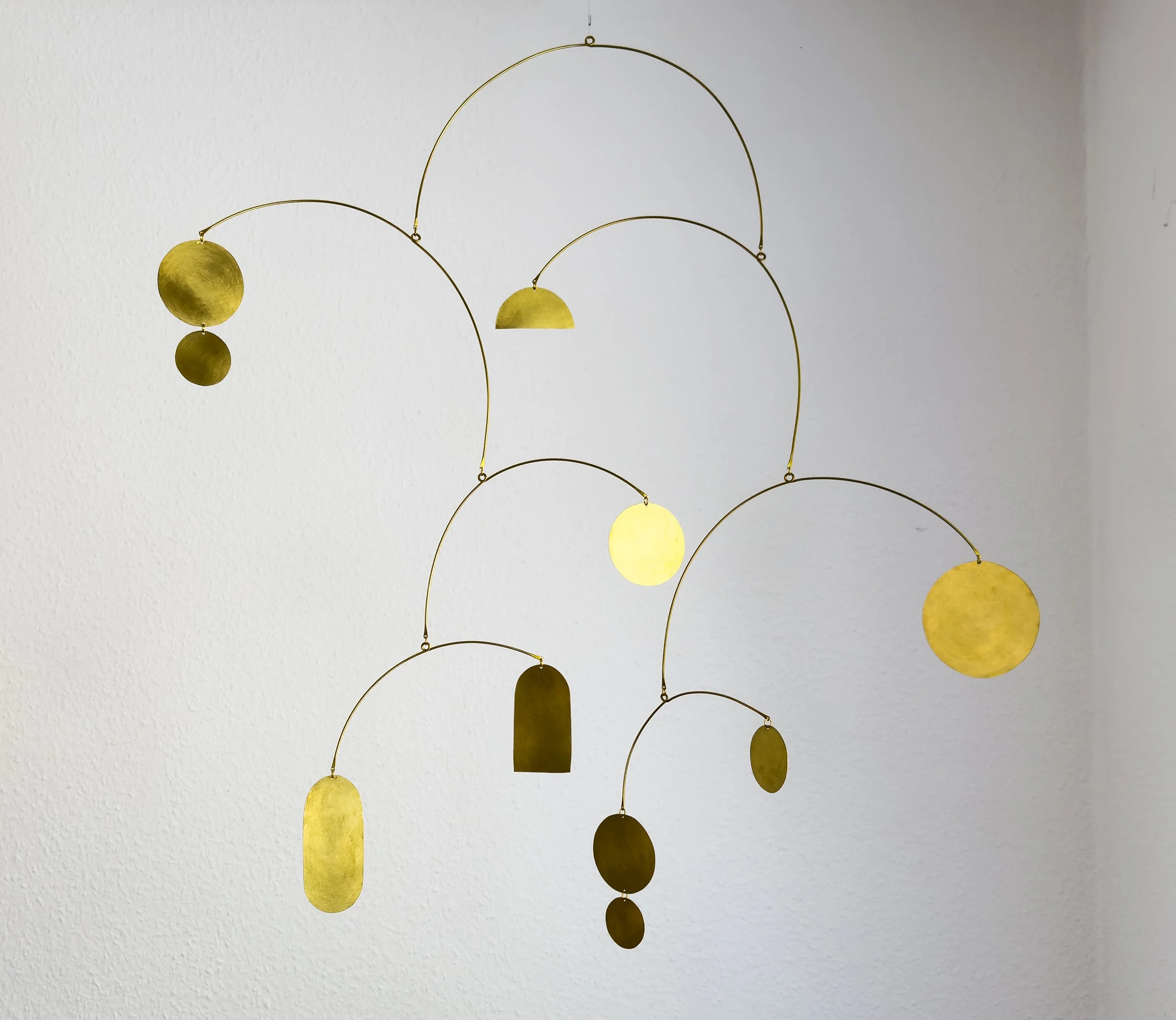 Ein Mobilé aus goldfarbenen Metallelementen vor einer weißen Wand. Unser System ist wie ein Mobilé. berührst du ein Element, deine Gedanken, deine Gefühle, deine Seele, kommt alles in Bewegung und richtet sich neu aus.