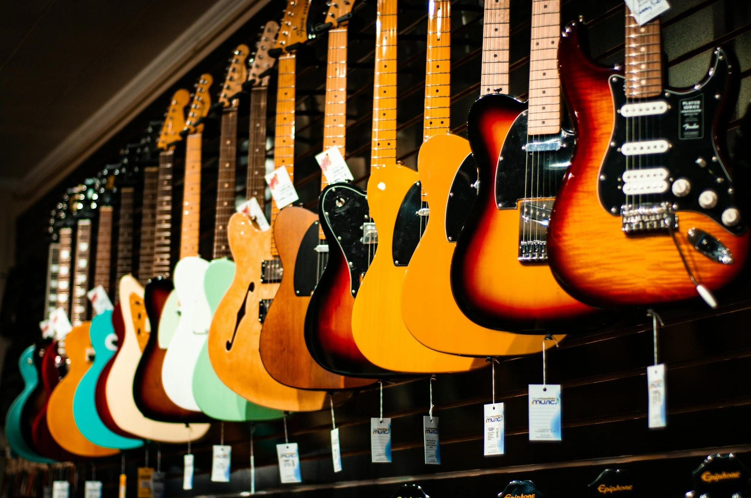 Displays a row of colorful electric and acoustic guitars hanging on a store wall.