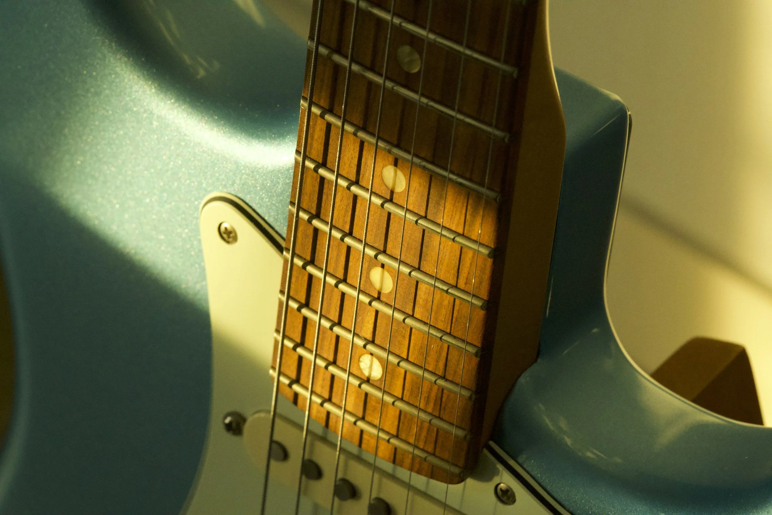 Close-up of an electric guitar's fretboard and strings, with a blue-green body and a wooden fretboard.