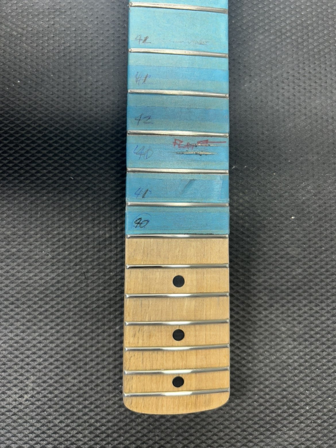 A guitar fretboard with markings indicating different fret positions, including 42, 44, and 40, with some markings in blue and red ink, and some frets made of wood and metal.