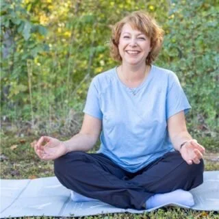 Chris McDonald, Licensed Professional Counselor, sitting cross-legged on a yoga mat in a meditation posture in front of green foliage