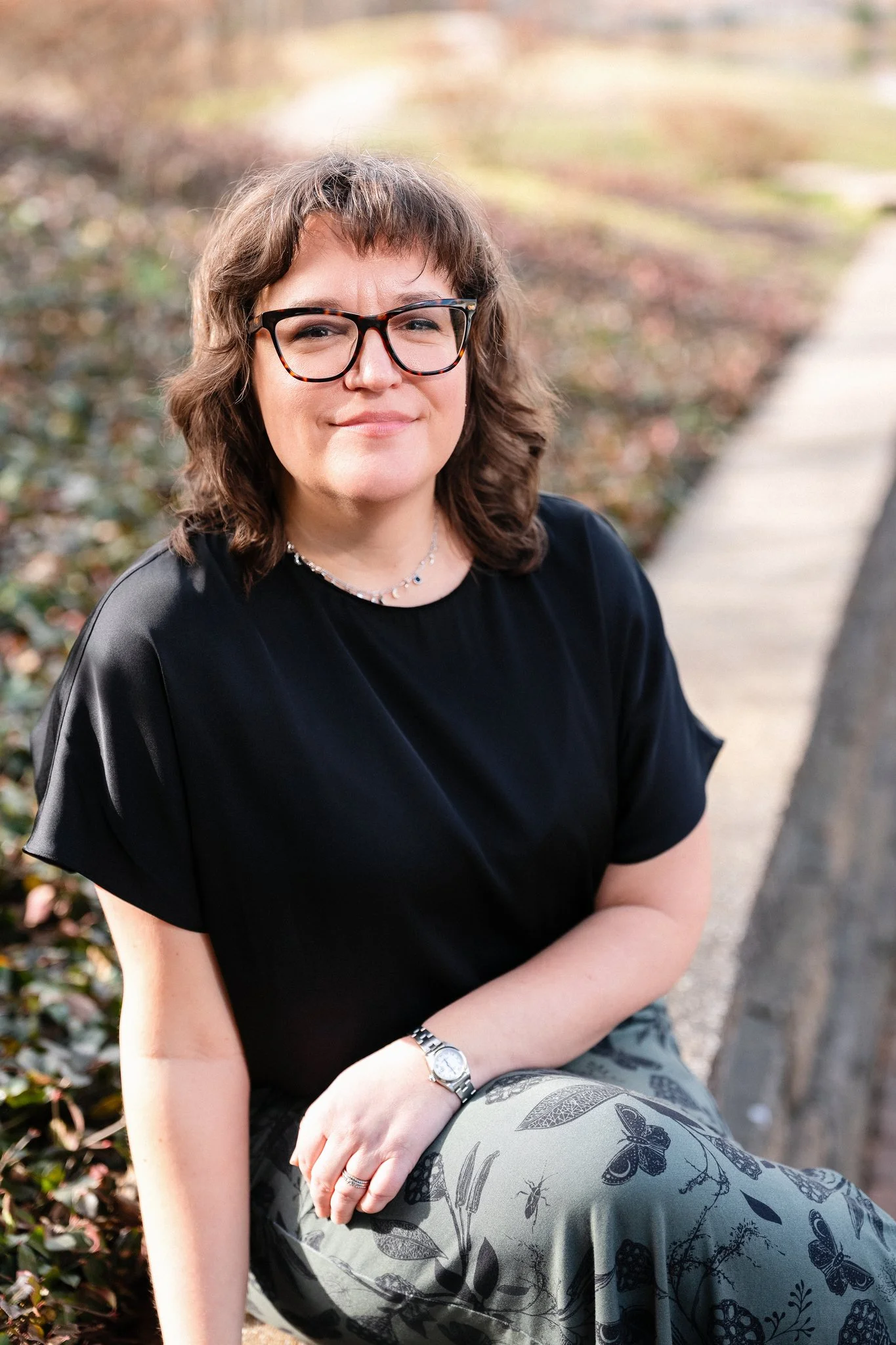 Lauren Burkart, Licensed Professional Counselor Associate and Certified Rehabilitation Counselor, sitting outside in a black shirt and glasses, smiling.