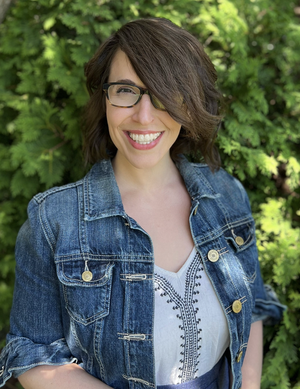 Niki Colon, Licensed Clinical Social Worker, smiling wearing a blue denim jacket in front of a green hedge.