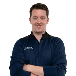 David McGettigan, pain and movement specialist, smiling wearing a navy blue quarter-zip pullover with his arms crossed