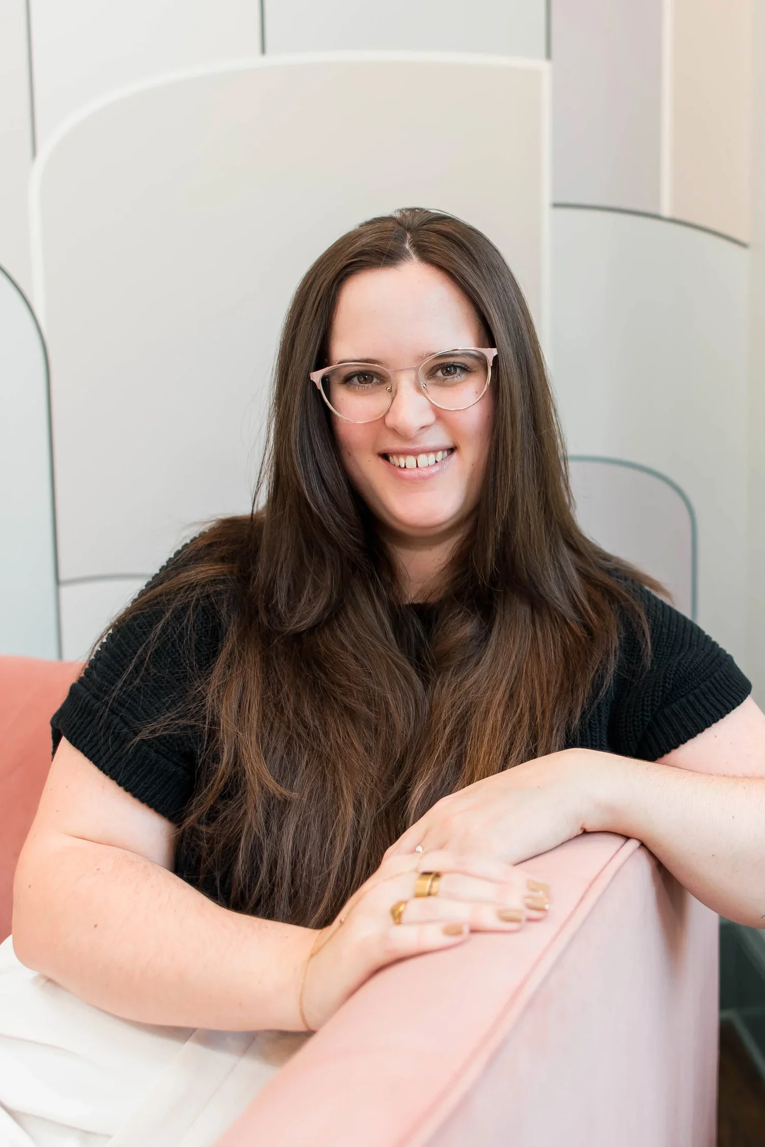 Destiny Davis, Licensed Professional Counselor and Certified Rehabilitation Counselor, sitting on a pink couch in a black shirt, wearing glasses, smiling.