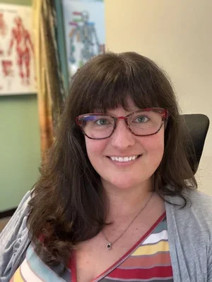 Kelly Clark, Licensed Physical Therapist and founder, wearing a multicolored striped shirt and a grey cardigan