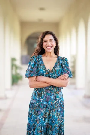 Rita Gupta, board-certified family and integrative medicine physician (DO), smiling wearing a blue floral patterned dress with her arms crossed
