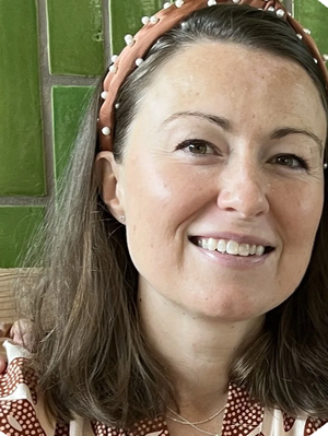 Sarah Stasica, LMSW, smiling wearing a pearl-embellished headband against a green tiled background