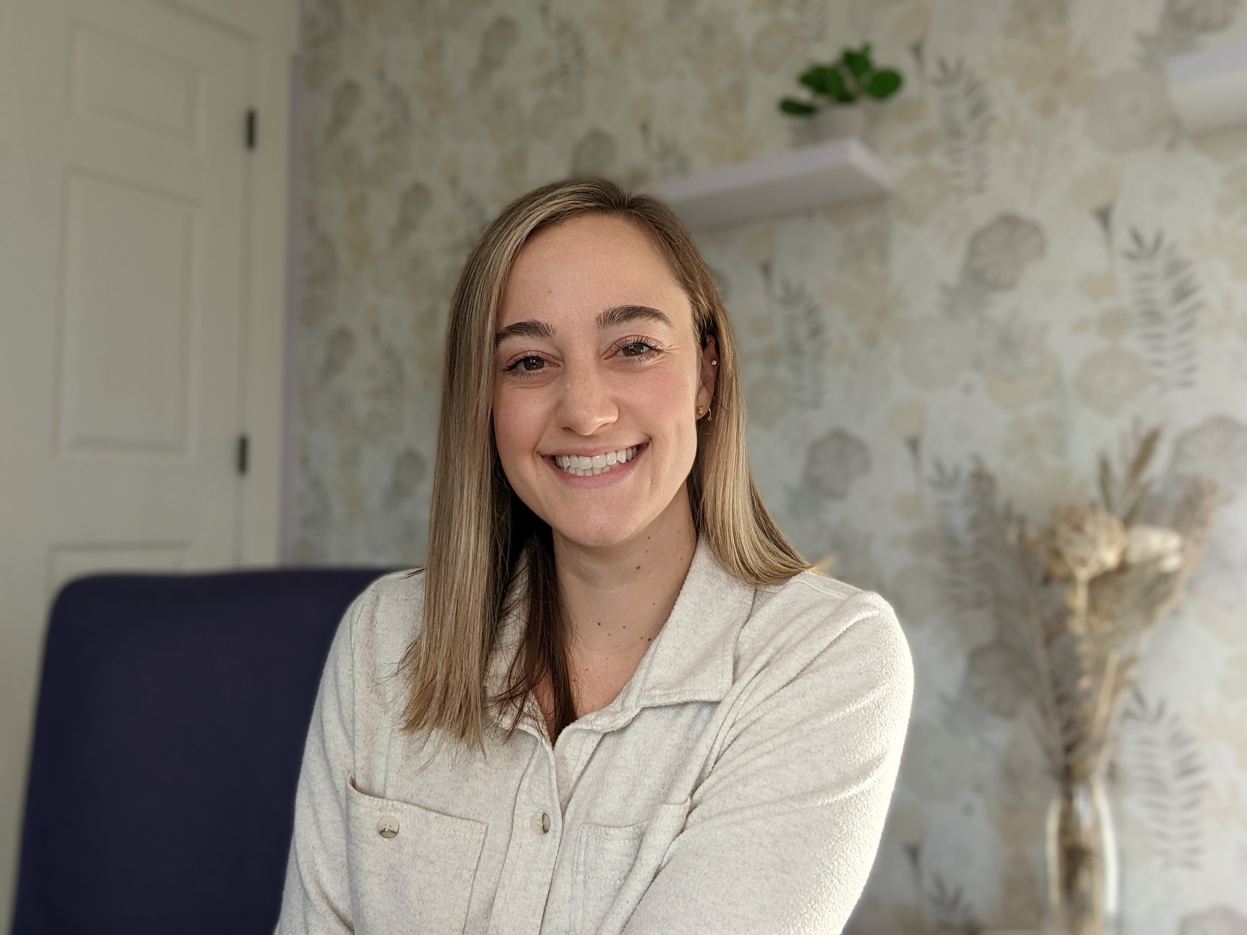 Lexi Gross, Licensed Professional Counselor, smiling wearing a cream-colored collared top against a soft floral wallpaper background