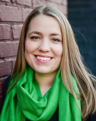 Joy Johnson with long straight hair wearing a vibrant green scarf in front of a brick background.