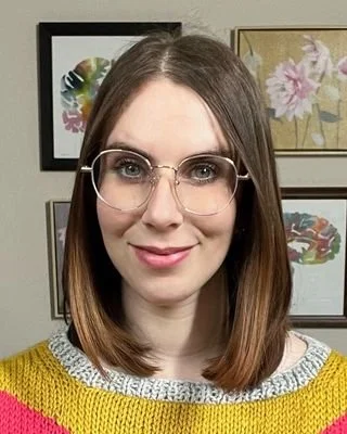 Rachelle Friedman, Licensed Clinical Social Worker, smiling in a vibrant knit sweater in front of framed wall art