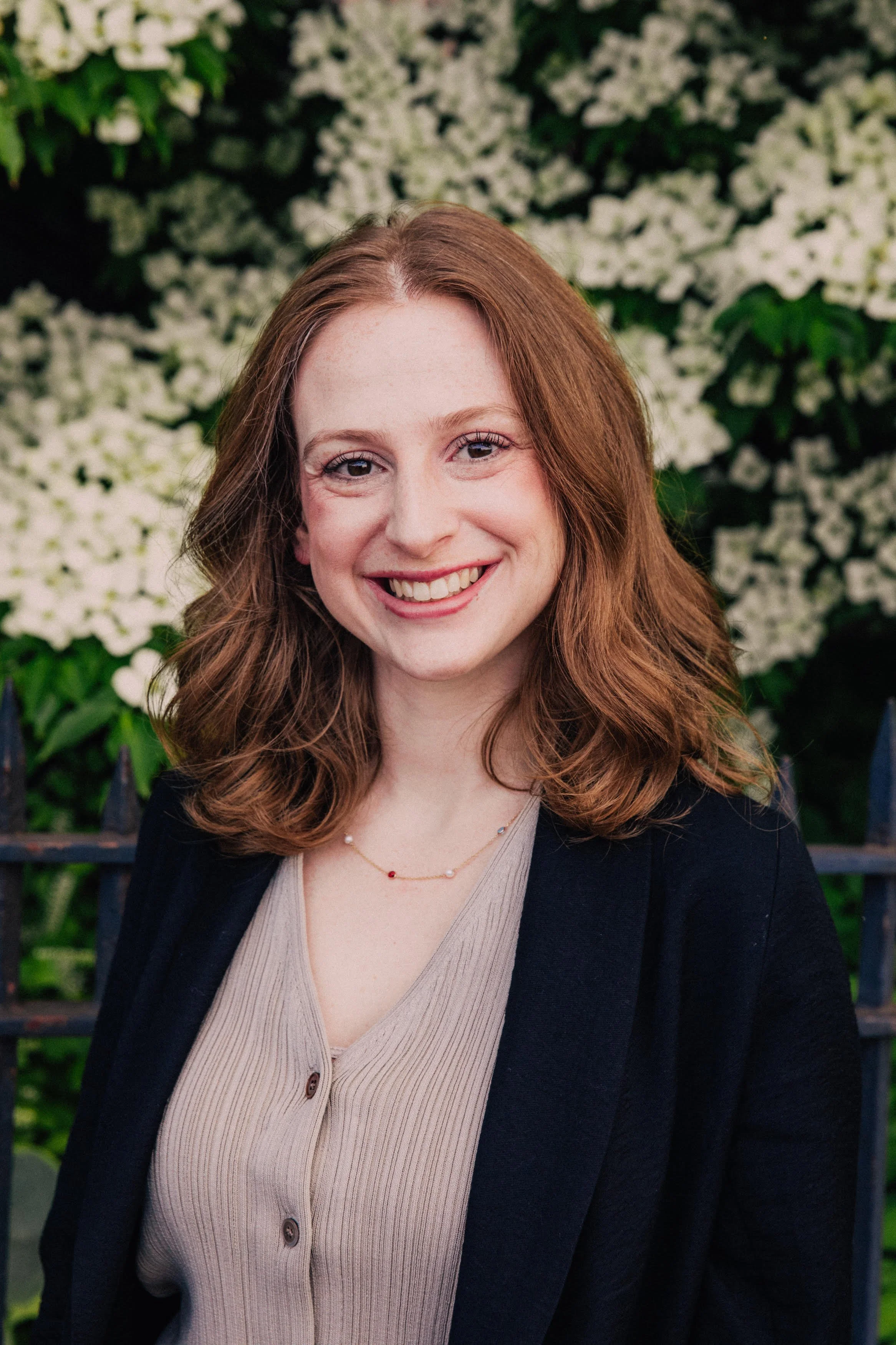 Ariel Katz, Licensed Mental Health Counselor, smiling in a beige knit top and black blazer in front of blooming white flowers