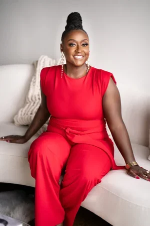 Brentia Caldwell, Licensed Professional Counselo, Certified Professional Counselor Supervisor and founder, smiling wearing a vibrant red jumpsuit while sitting on a white sofa