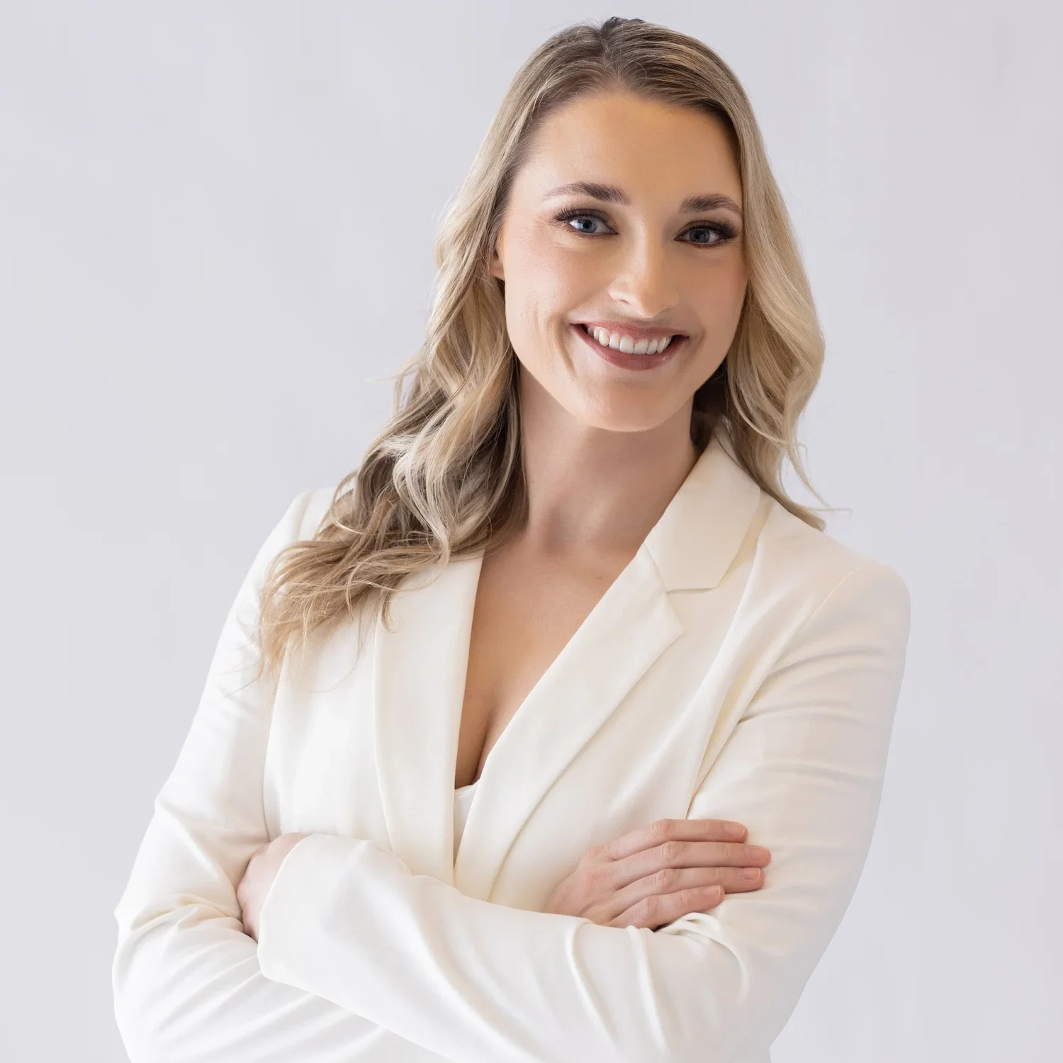 Kelsey Ruffing, a licensed therapist and founder, smiling wearing a white blazer with her arms crossed