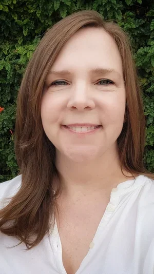 Jackie Williams-Reade, Licensed Marriage and family therapist, smiling wearing a white buttoned shirt in front of a green hedge