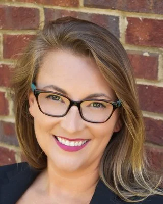 Jennifer Hama, Licensed Professional Counselor and author, smiling in a dark suit jacket in front of an exposed brick wall