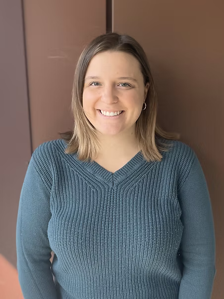 Rachael Gay, Licensed Clinical Social Worker, smiling in a ribbed teal V-neck sweater against a brown backdrop