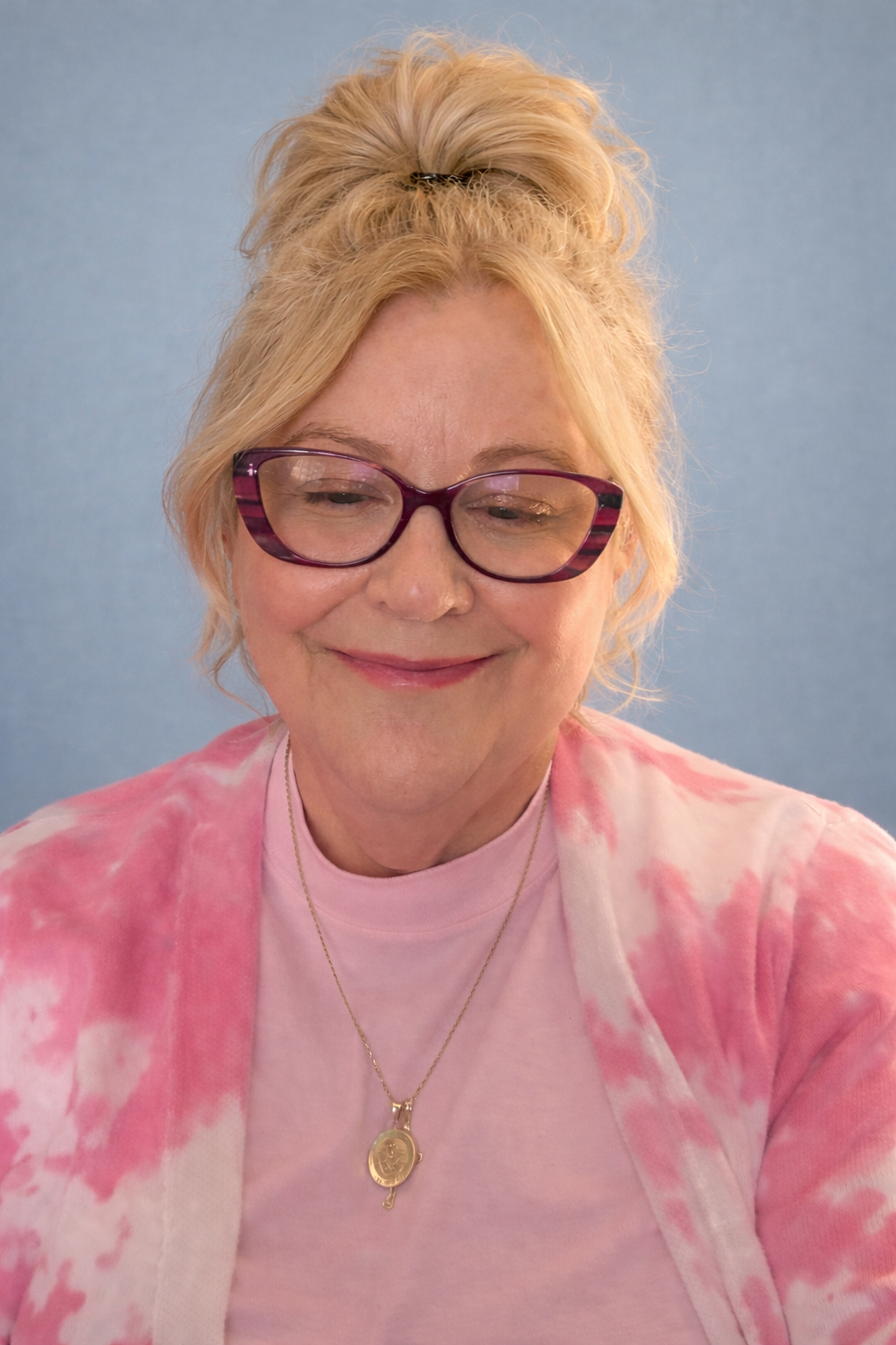 Tammi Imel, Licensed Professional Counselor, smiling wearing purple glasses and a pink tie-dye cardigan against a plain blue backdrop