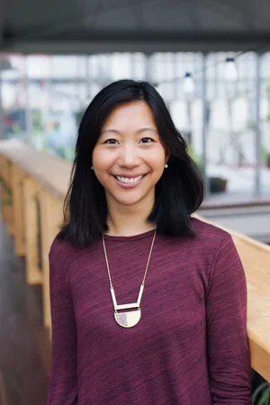 Tiffany Yu, CEO, 3x TEDx speaker and author, smiling wearing a maroon long-sleeved shirt and a gold geometric pendant necklace