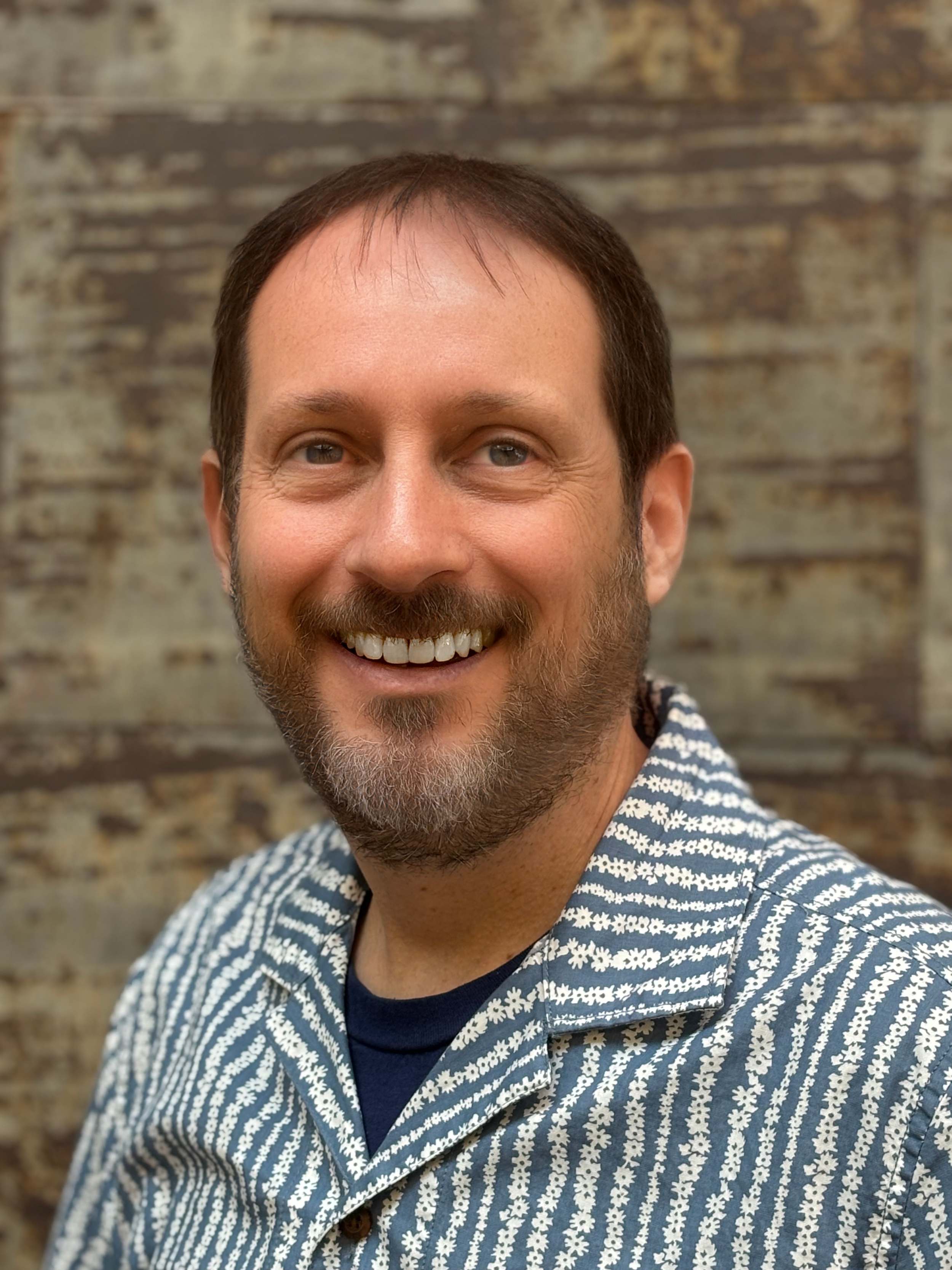 Matthew Reeves, Licensed Professional Counselor and Certified Rehabilitation Counselor, smiling in a blue and white patterned shirt against a rustic wood wall.