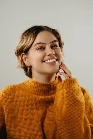 Faith Davis, freelance science, smiling in a yellow turtleneck sweater and touching her jawline
