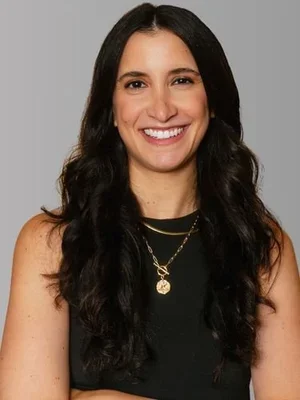 Dr. Antonia Repollet, Licensed Clinical Psychologist and Certified School Psychologist, smiling wearing a black sleeveless top and layered gold necklaces against a solid grey background