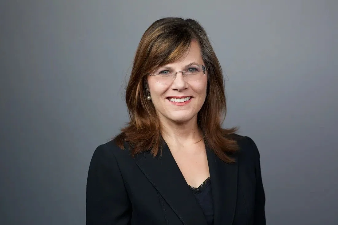 Dr. Robin McFarlane, expert in sleep and psychology, smiling in a black blazer against a gray backdrop
