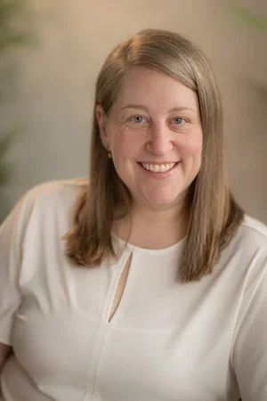 Headshot portrait of Laurie Dos Santos, Clinical Psychologist and founder of Evolvinn Therapy and Consulting, smiling in a white top