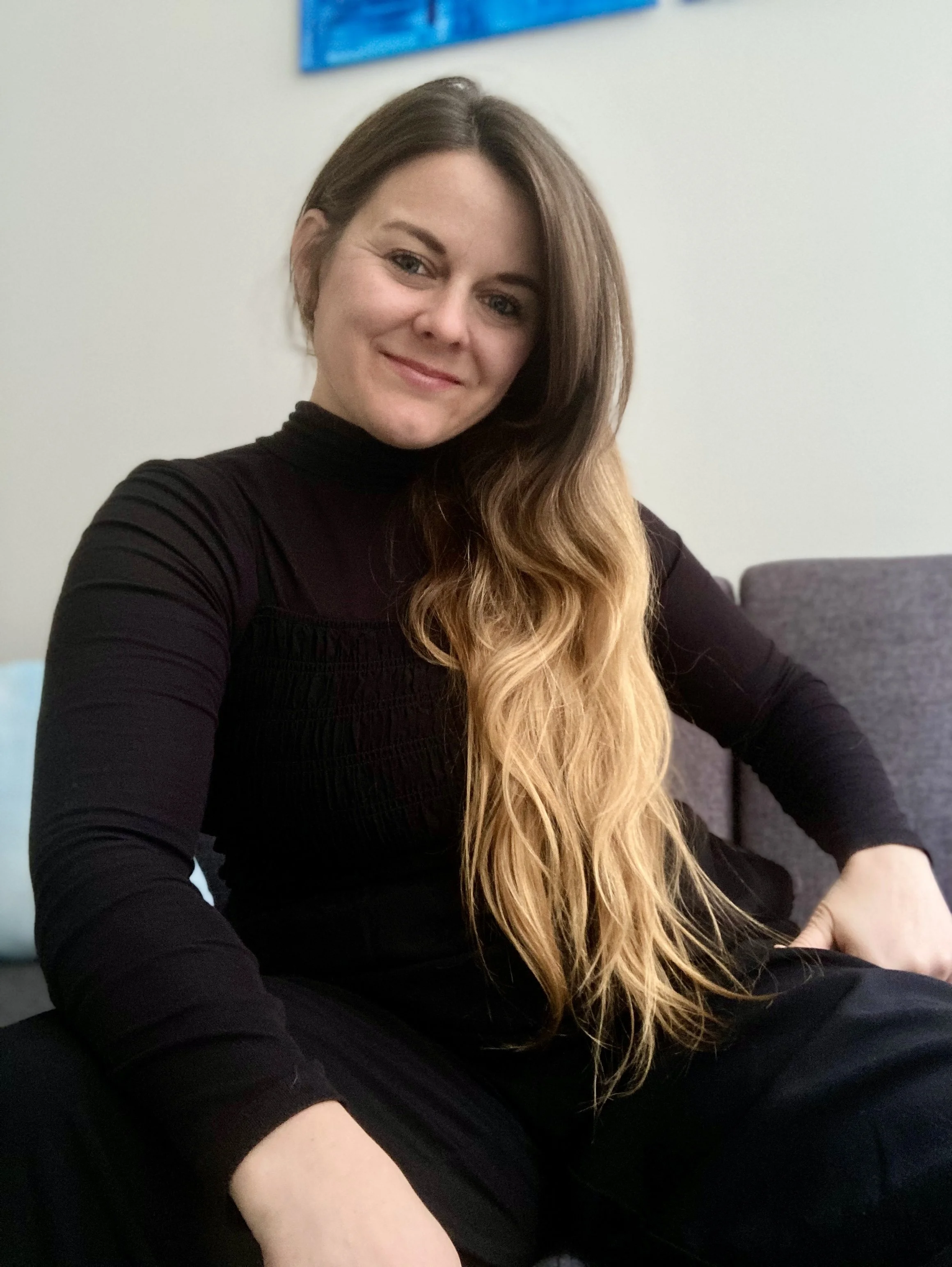 Shannon Schureman, Licensed Mental Health Counselor, smiling in a black long-sleeved top sitting on a couch indoors
